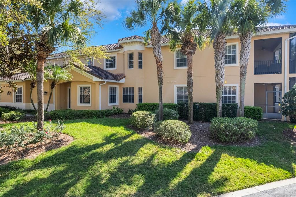A two-story tan apartment building with a tile roof and palm trees in the front — 54 CAMINO REAL BOULEVARD UNIT 504, HOWEY IN THE HILLS, FL