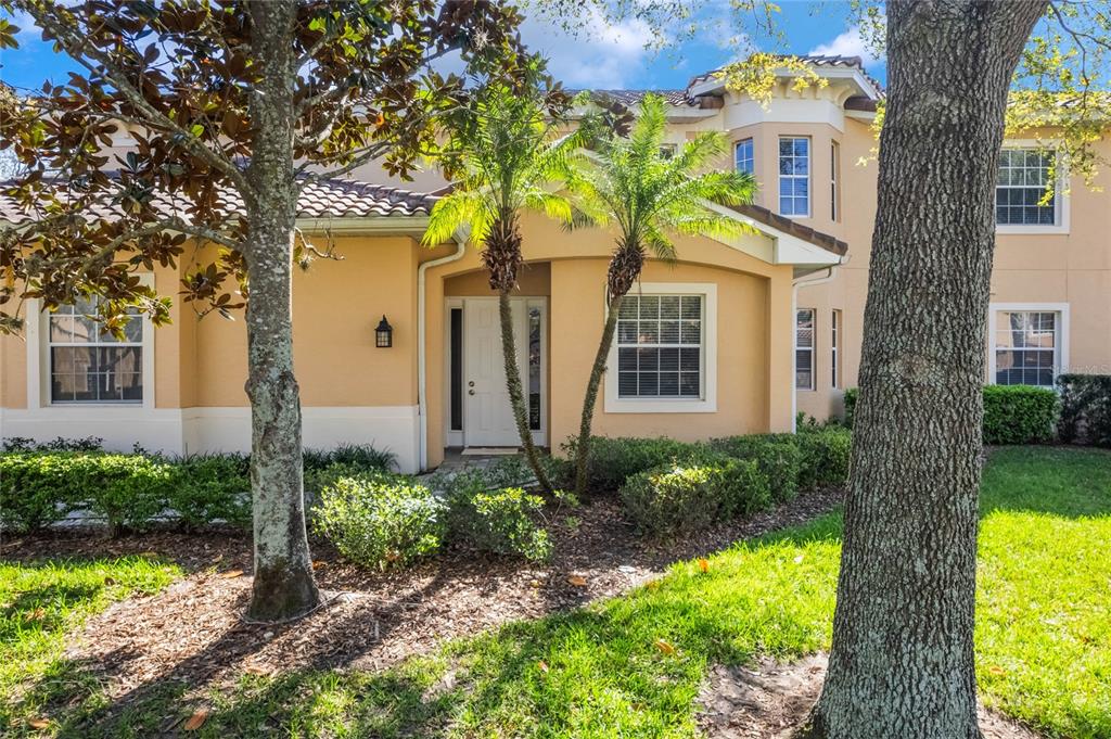 The exterior of a two-story tan stucco house features a front entrance with palm trees — 54 CAMINO REAL BOULEVARD UNIT 504, HOWEY IN THE HILLS, FL