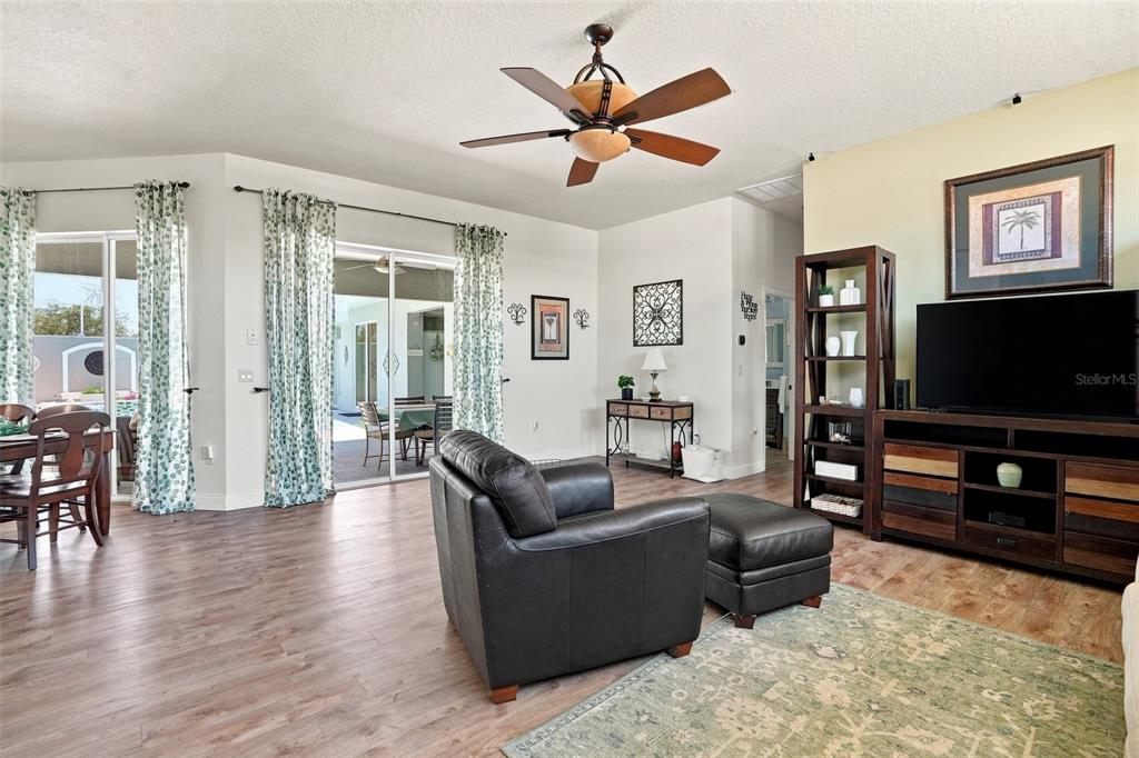 A living room features wood-look flooring, a ceiling fan, a television console, and sliding doors — 11399 REDGATE STREET, SPRING HILL, FL