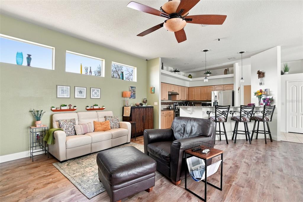 An open-concept living room features a beige sofa, leather armchair, and kitchen with bar seating — 11399 REDGATE STREET, SPRING HILL, FL