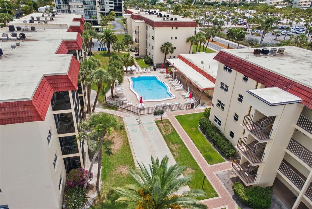 An aerial view shows a swimming pool nestled between multi-story apartment buildings with palm trees — 915 BEACH ROAD UNIT 318, SARASOTA, FL