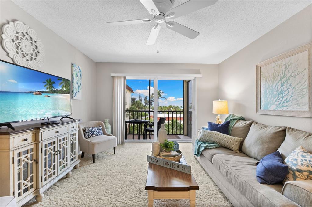 A living room features a beige sofa, a white media console, and a balcony view — 915 BEACH ROAD UNIT 318, SARASOTA, FL