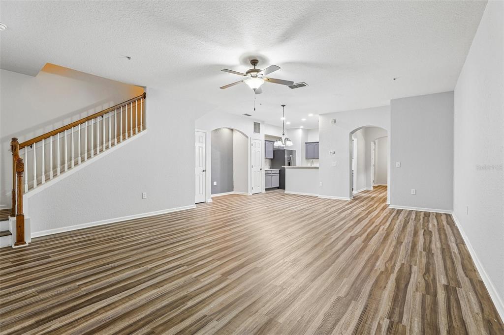 An open-concept living area features wood-look flooring, a staircase with a wooden railing, and a kitchen — 14261 TURNING LEAF DRIVE, ORLANDO, FL