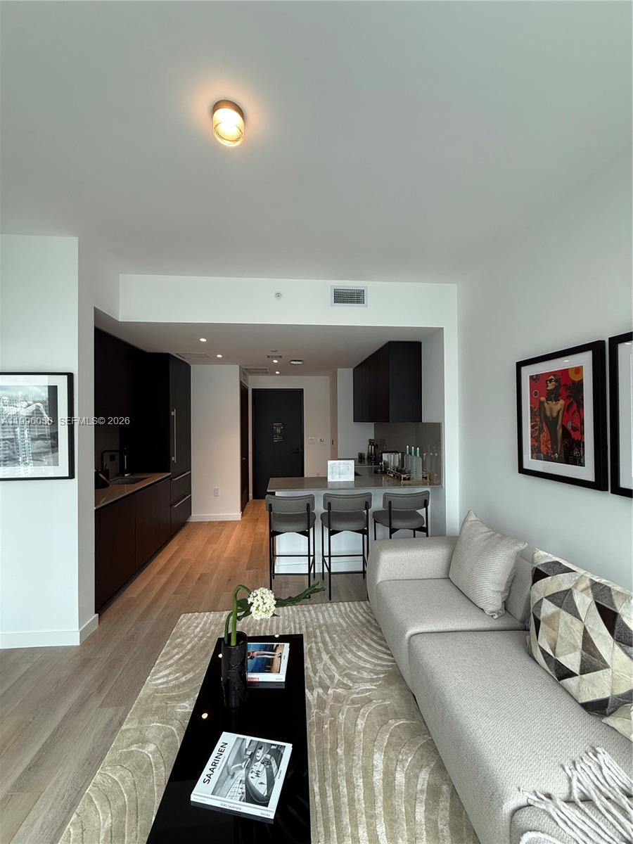 A modern living room and kitchen area with dark cabinetry, bar seating, and neutral furniture — 20 NE 11th St # 2909, Miami FL 33132, MIAMI, FL