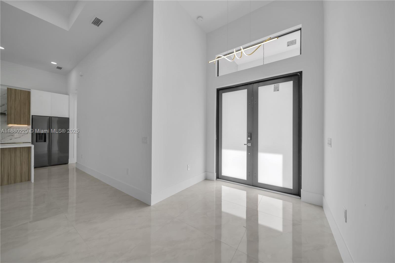 A modern entryway features white walls, large floor tiles, and double glass doors — 1913 IRVING AVE, Lehigh Acres FL 33972, LEHIGH ACRES, FL