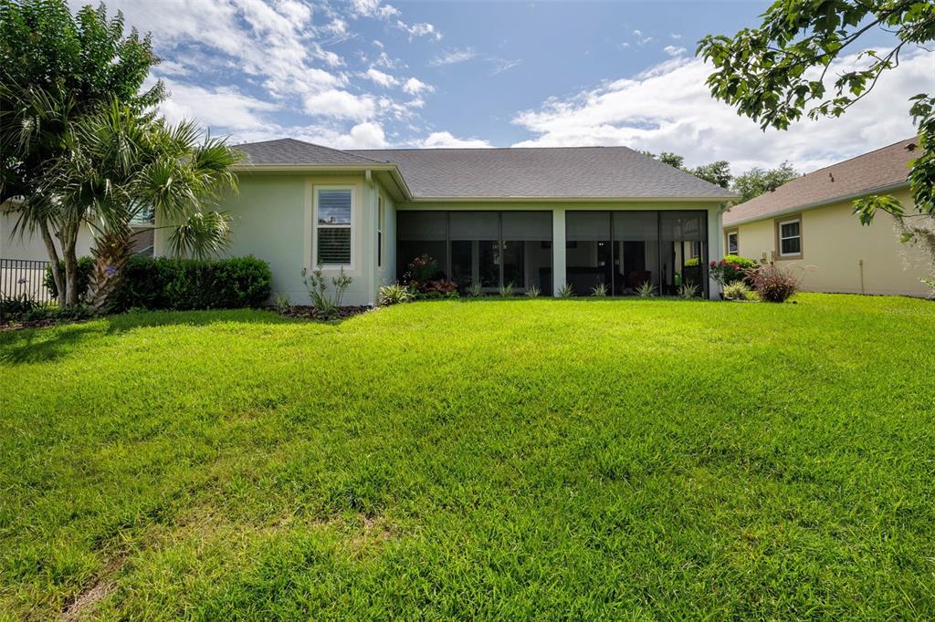 The backyard of a light green house features a screened-in porch and a grassy lawn — 309 BELLINGRATH TERRACE, DELAND, FL