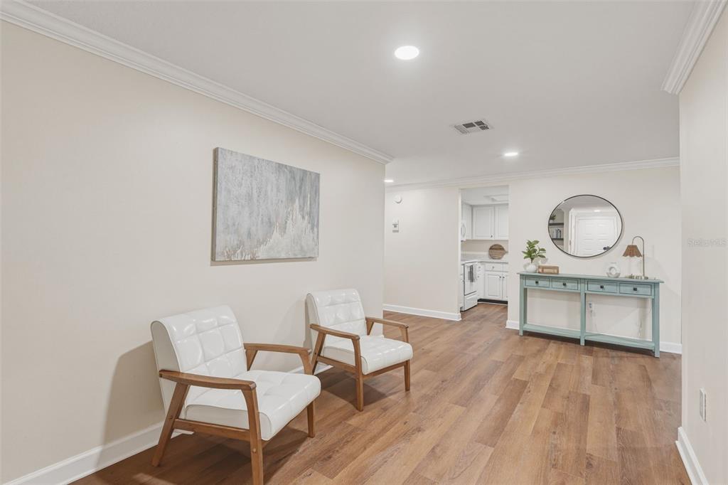 A room with wood-look flooring features two white chairs, a console table, and wall art — 1411 STRADA D ARGENTO, VENICE, FL