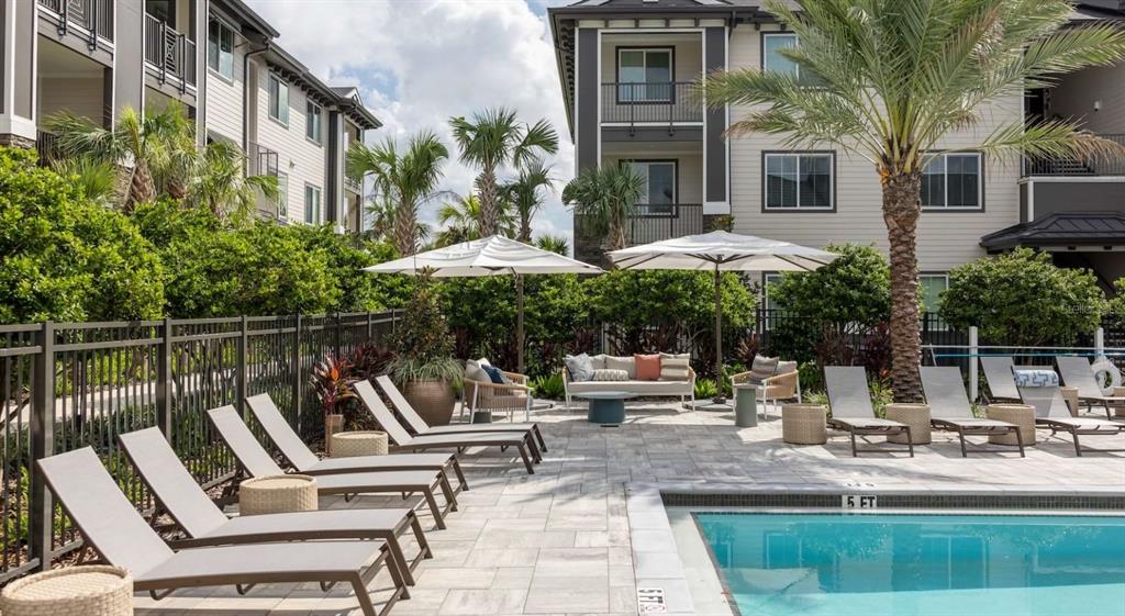 An outdoor swimming pool area with lounge chairs, umbrellas, and patio furniture at an apartment complex — 5000 COLLINA TERRACE UNIT A2, CLERMONT, FL