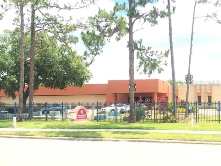 A low-rise commercial building with an orange facade sits behind a black metal fence — 6177 LAKE ELLENOR DRIVE, ORLANDO, FL