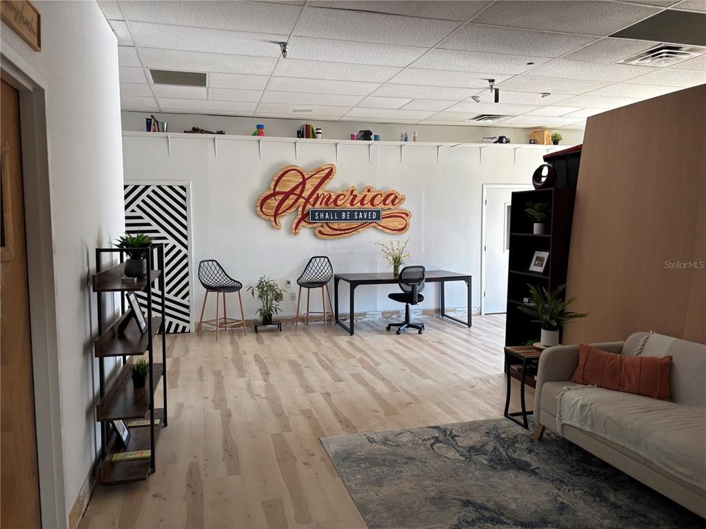 An office space features light wood flooring, a wall sign, a desk, and a sofa — 6177 LAKE ELLENOR DRIVE, ORLANDO, FL