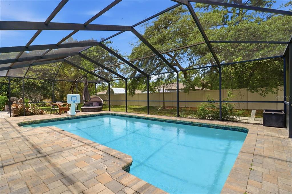 A swimming pool with a paved deck is enclosed by a screened lanai in a backyard — 8720 N TROJAN DRIVE, CITRUS SPRINGS, FL