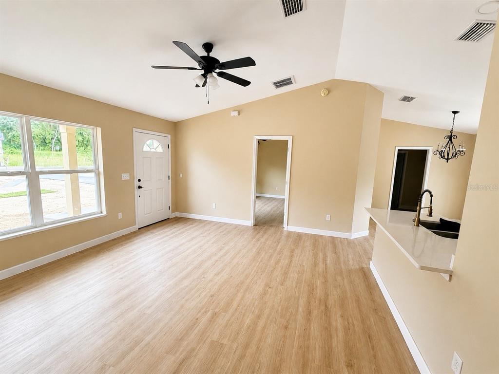 A living room with light wood-look flooring, a ceiling fan, and an open kitchen area — 9 LOCUST RUN, OCALA, FL