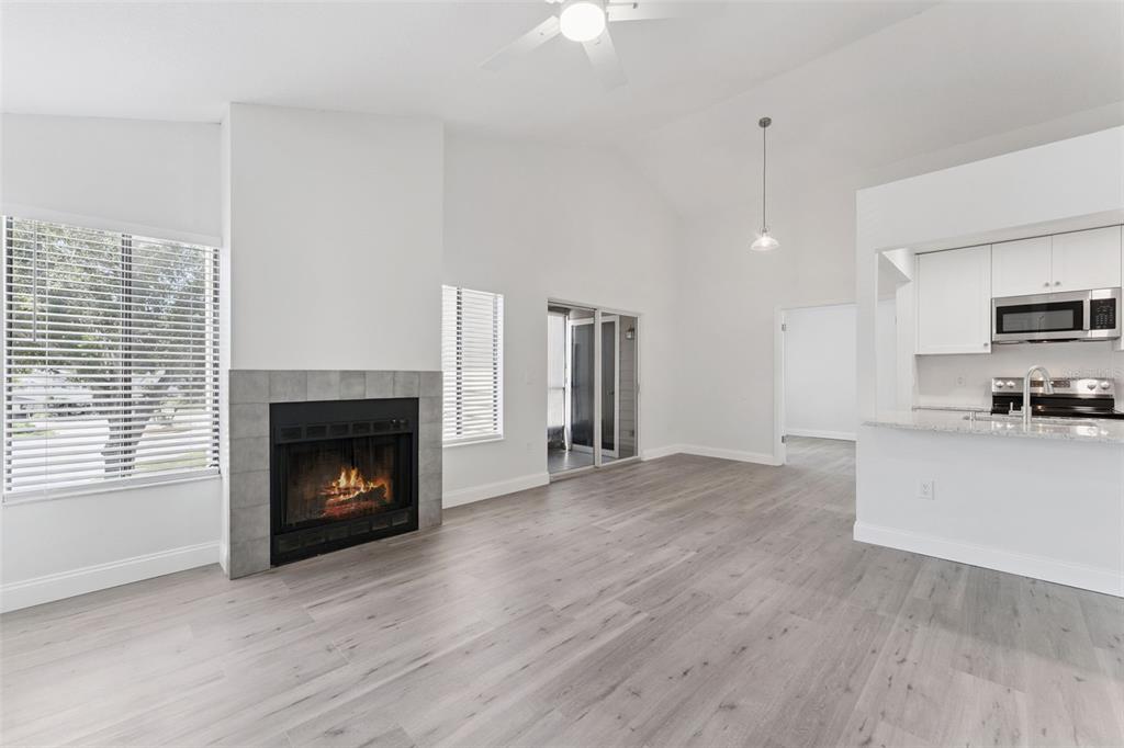 A living room with a fireplace, light wood flooring, and an adjacent kitchen — 549 SUN RIDGE PLACE UNIT 207, ALTAMONTE SPRINGS, FL