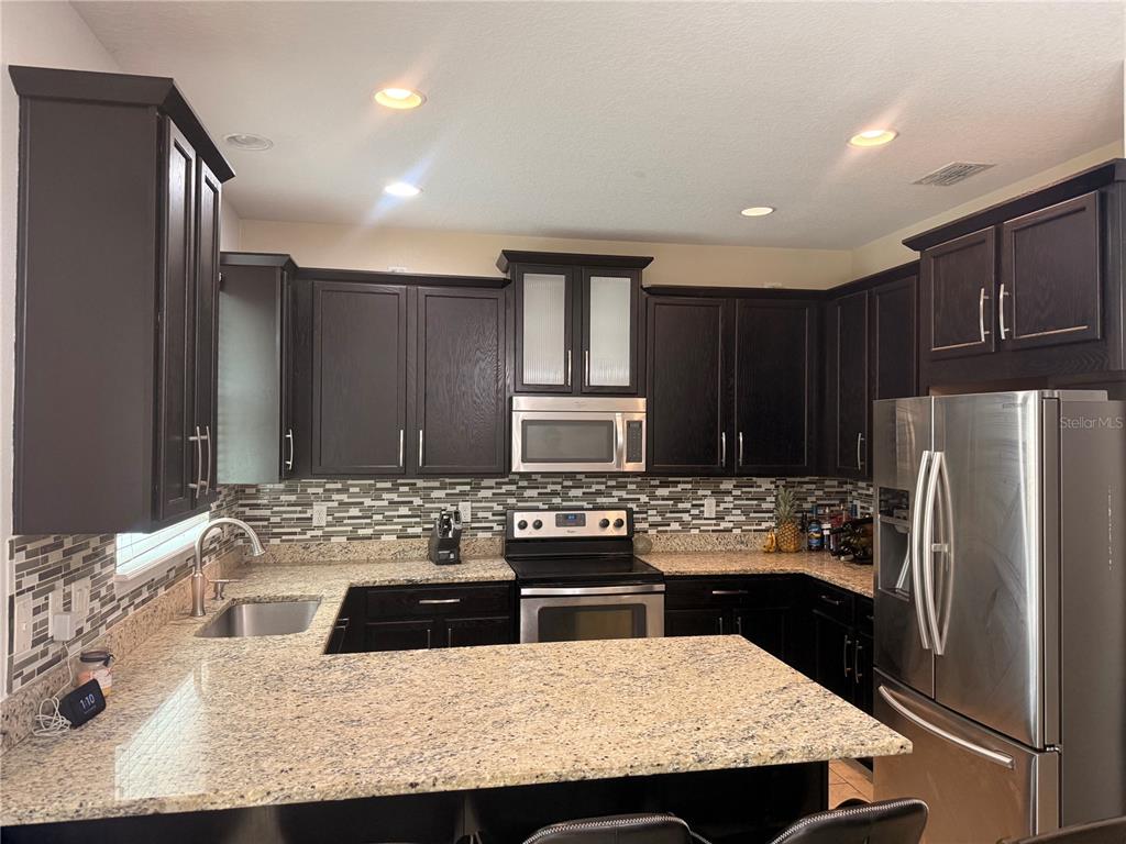 A kitchen features dark wood cabinets, granite countertops, stainless steel appliances, and a tiled backsplash — 2257 BROOKRIDGE TRAIL, SANFORD, FL