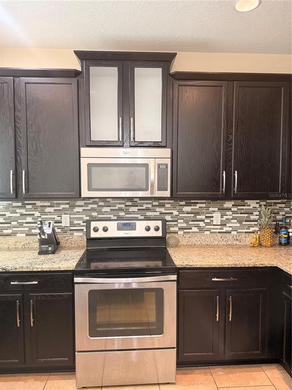 A kitchen features dark wood cabinets, stainless steel appliances, and a mosaic tile backsplash — 2257 BROOKRIDGE TRAIL, SANFORD, FL