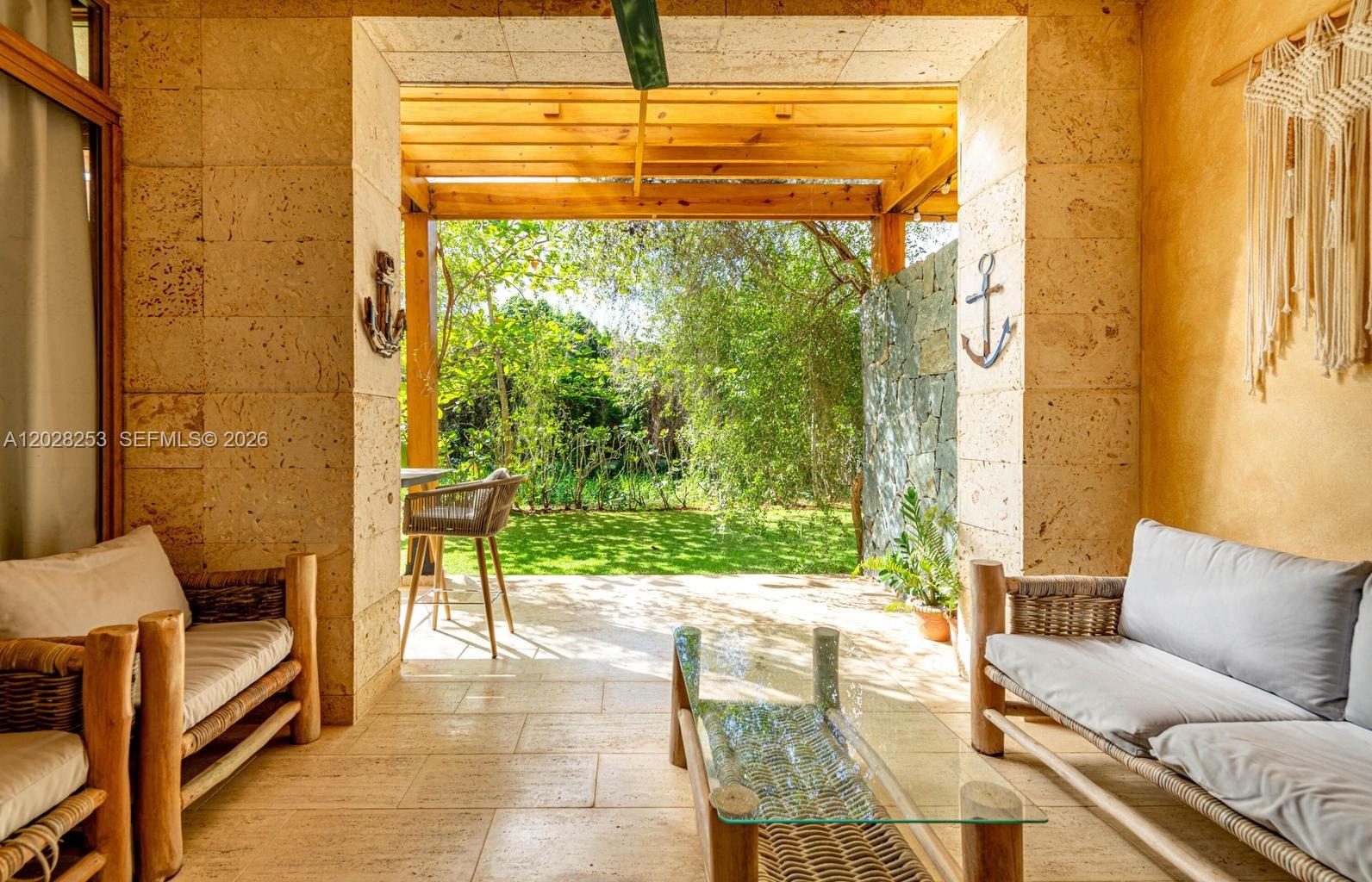 A covered stone patio features wicker furniture, a glass coffee table, and a garden view — FL