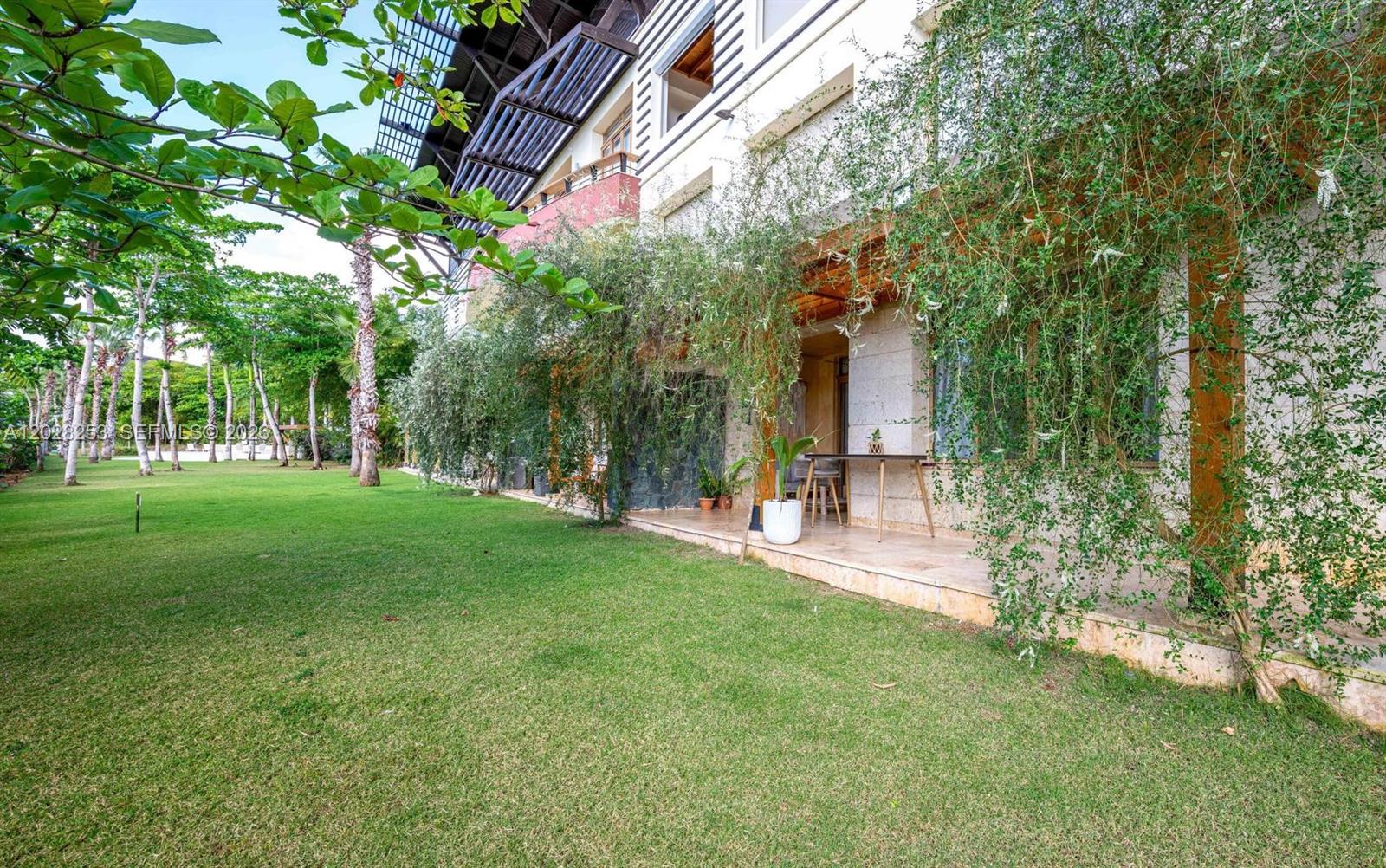 A patio with a table and chairs sits beside a grassy lawn and trees — FL