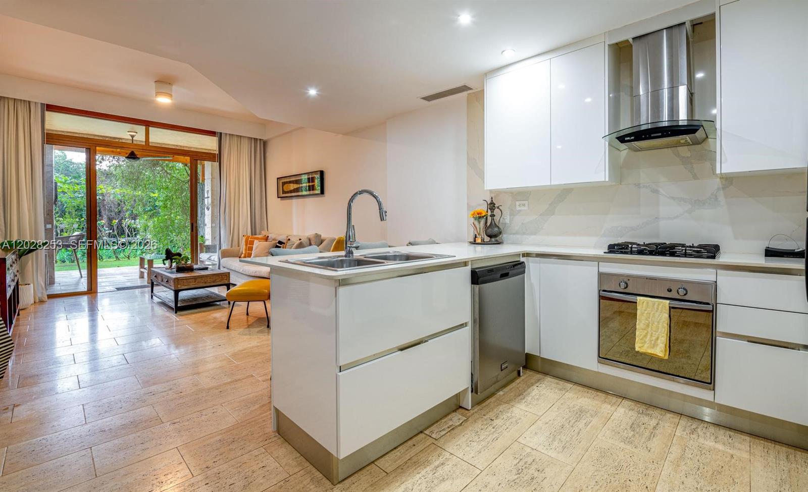 A modern kitchen with white cabinets and stainless steel appliances opens to a living area — FL