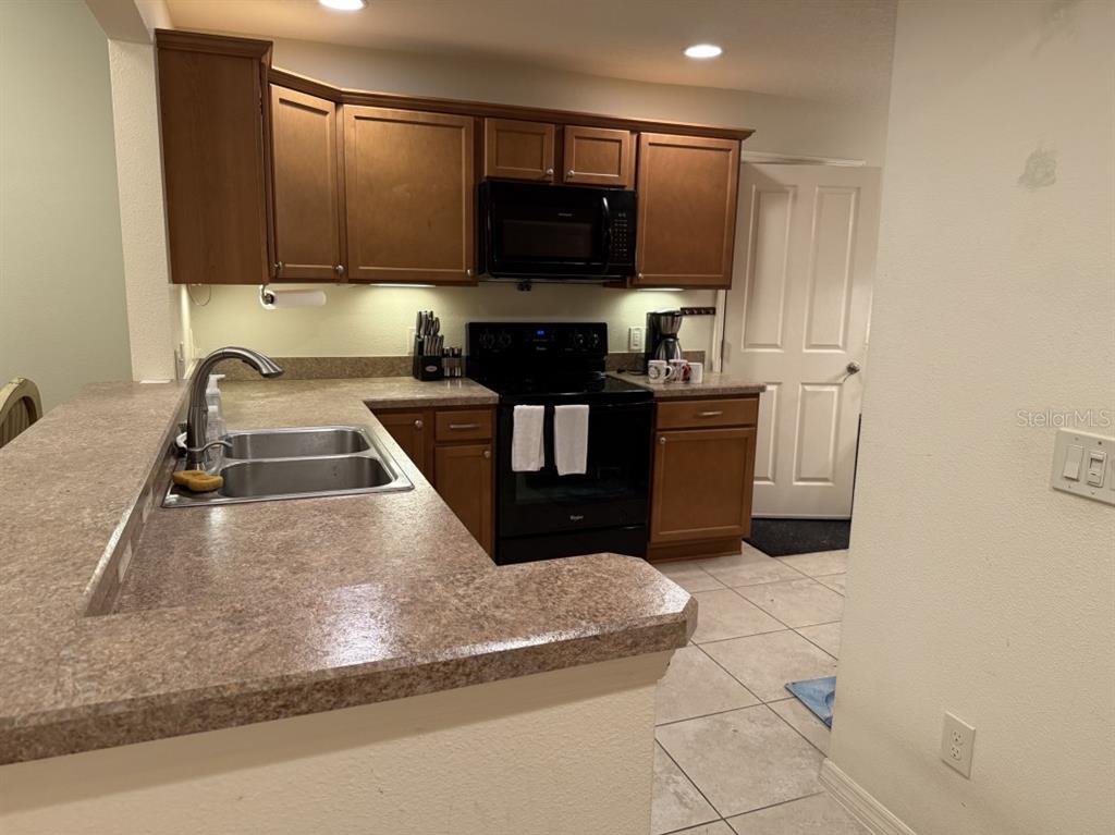 A kitchen features wood cabinets, black appliances, a double sink, and laminate countertops — 1097 HOLLYHOCK WAY, THE VILLAGES, FL