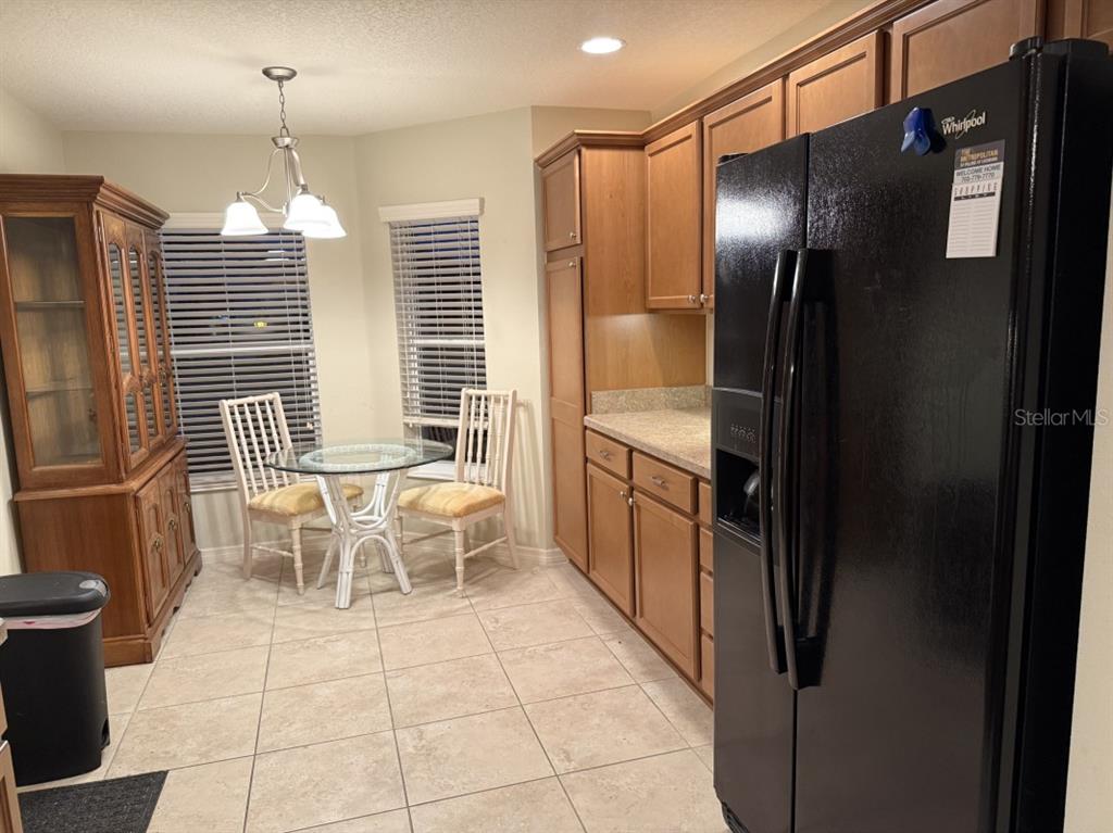 A kitchen with wood cabinets, a black refrigerator, and a small dining area with windows — 1097 HOLLYHOCK WAY, THE VILLAGES, FL