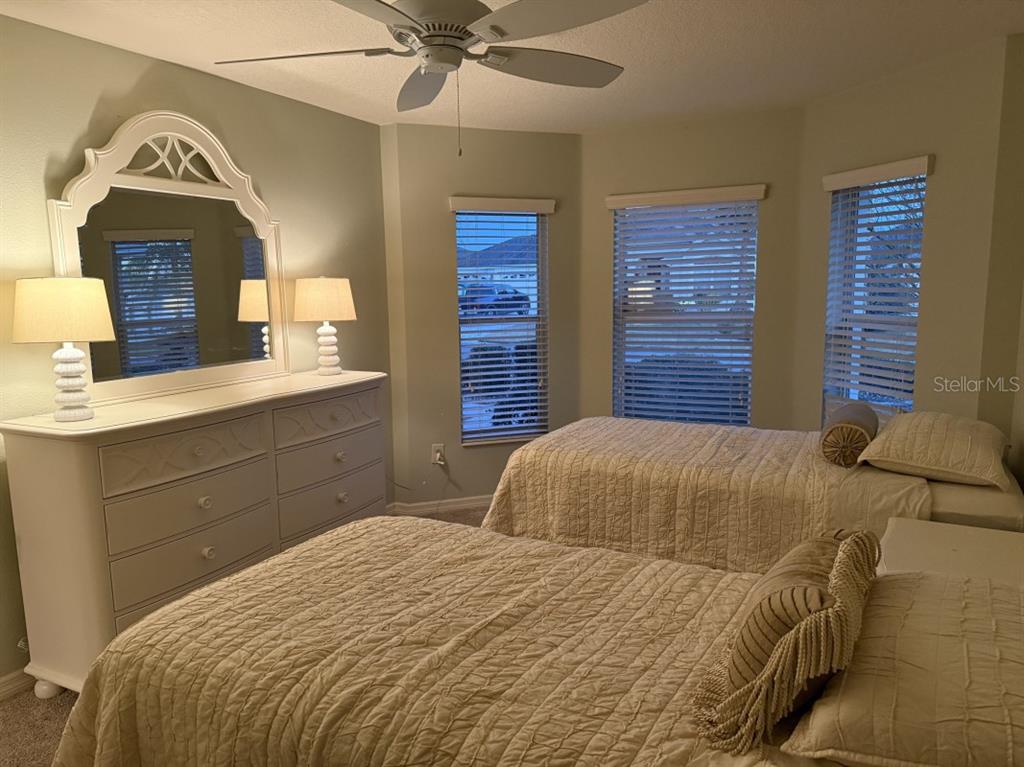 A bedroom features two beds, a white dresser with a mirror, and three windows — 1097 HOLLYHOCK WAY, THE VILLAGES, FL