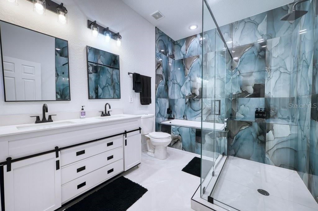 A modern bathroom features a double vanity, a glass-enclosed shower, and blue marble-patterned wall tiles — 158 CHICKERING STREET, PORT CHARLOTTE, FL