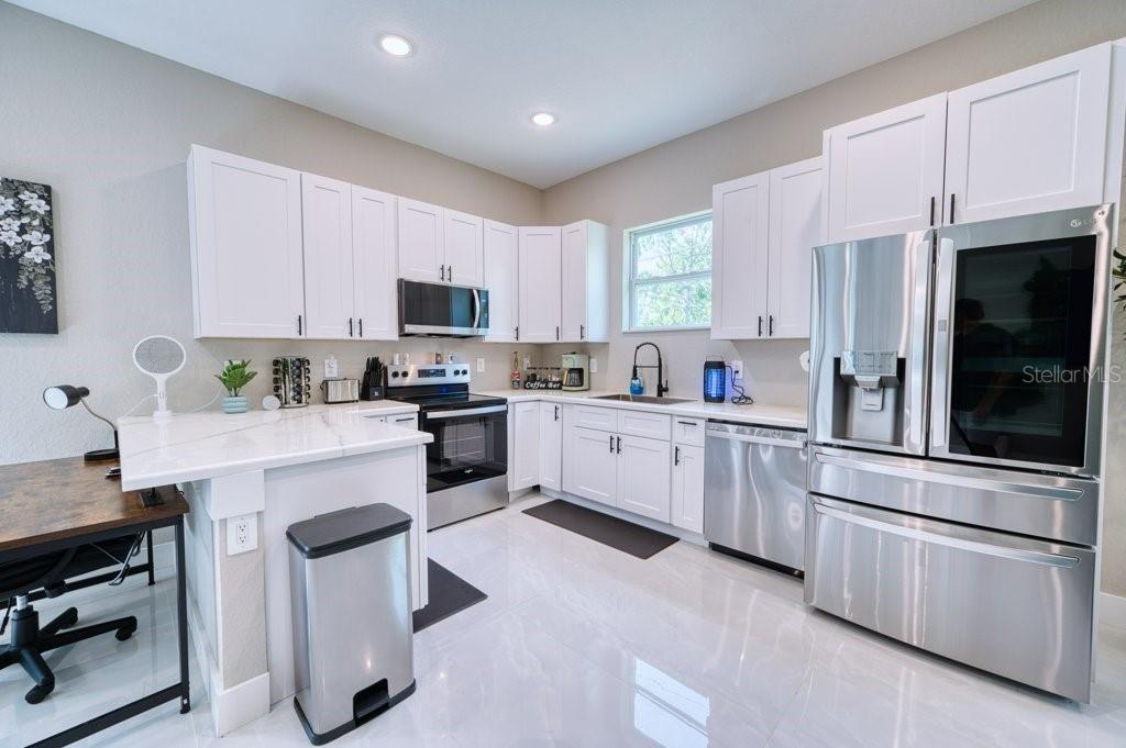 A modern kitchen features white cabinets, stainless steel appliances, and white countertops — 158 CHICKERING STREET, PORT CHARLOTTE, FL