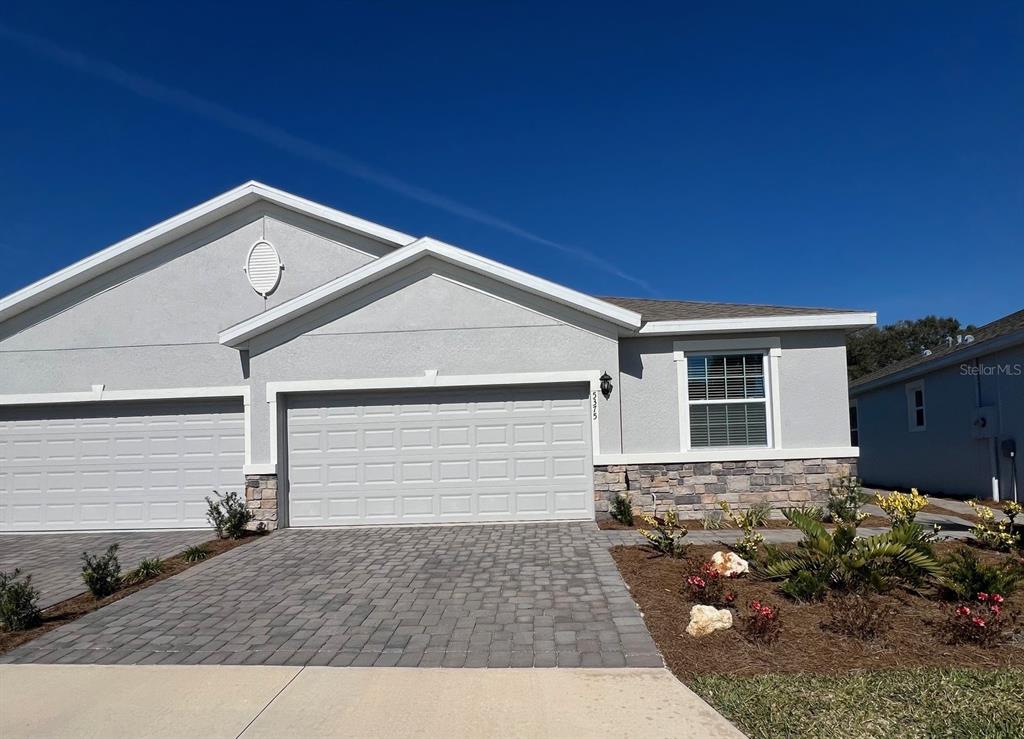 A gray stucco duplex with a stone facade, a paved driveway, and a two-car garage — 5375 NW 48TH PLACE, OCALA, FL