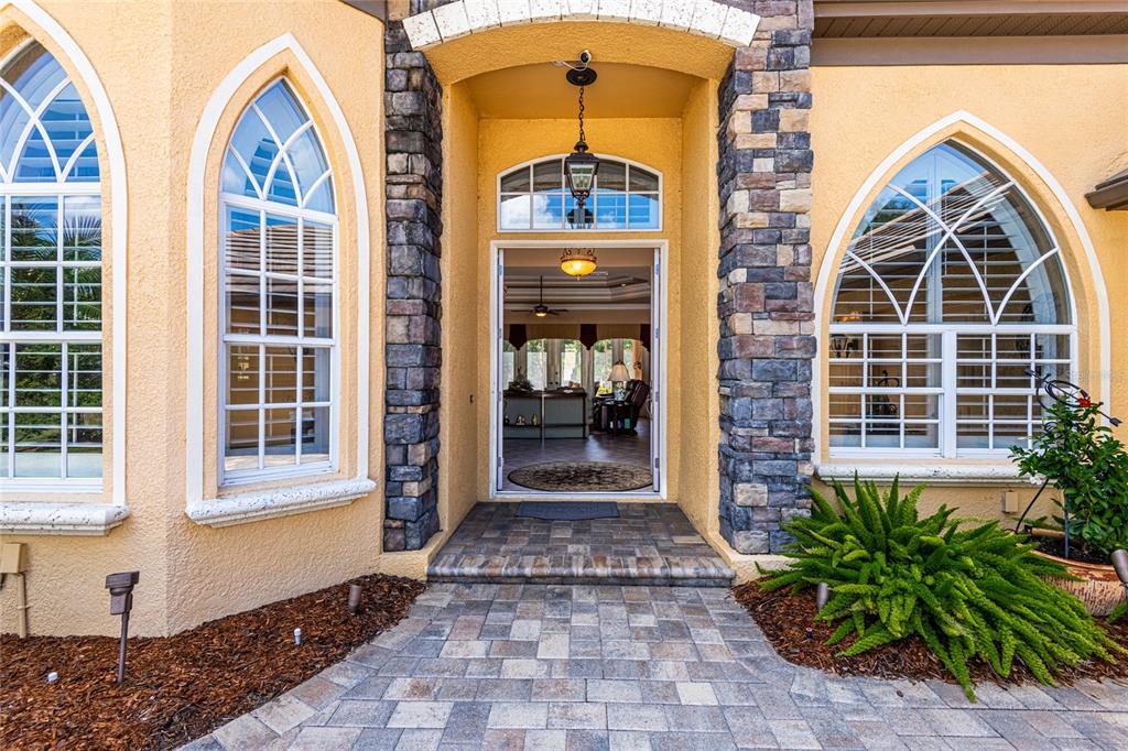 The front entrance of a stucco home features stone pillars, arched windows, and a paved walkway — 13152 TRADITION DRIVE, DADE CITY, FL