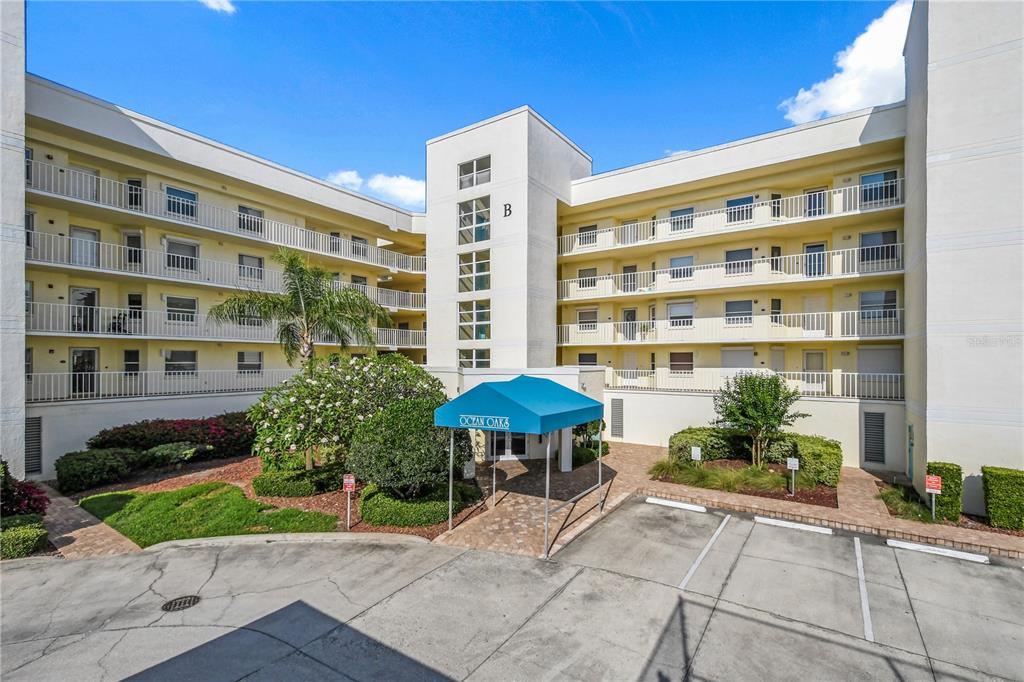 The exterior of a multi-story apartment building features a blue awning over the main entrance — 8700 RIDGEWOOD AVENUE UNIT B204, CAPE CANAVERAL, FL