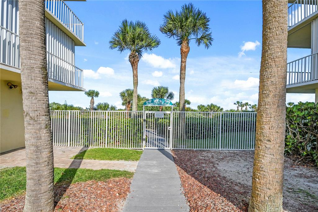 A concrete walkway leads to a gated entrance between two buildings with palm trees — 8700 RIDGEWOOD AVENUE UNIT B204, CAPE CANAVERAL, FL