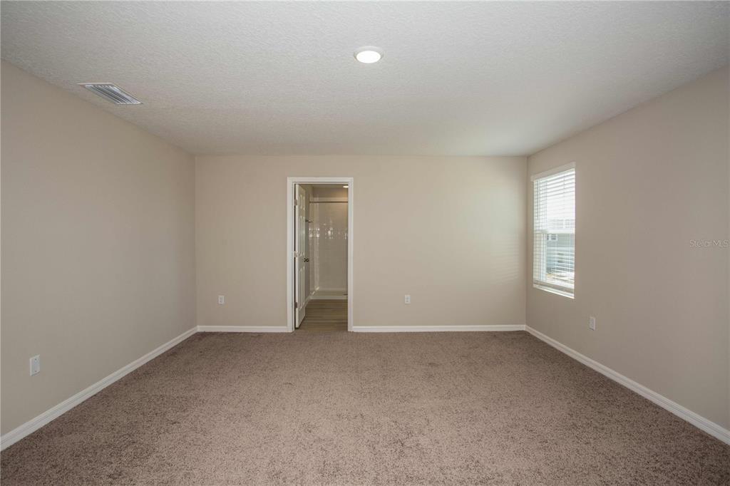 A carpeted bedroom features beige walls, a single window, and a doorway leading to a bathroom — 5390 SAN PIETRO DRIVE, WINTER HAVEN, FL