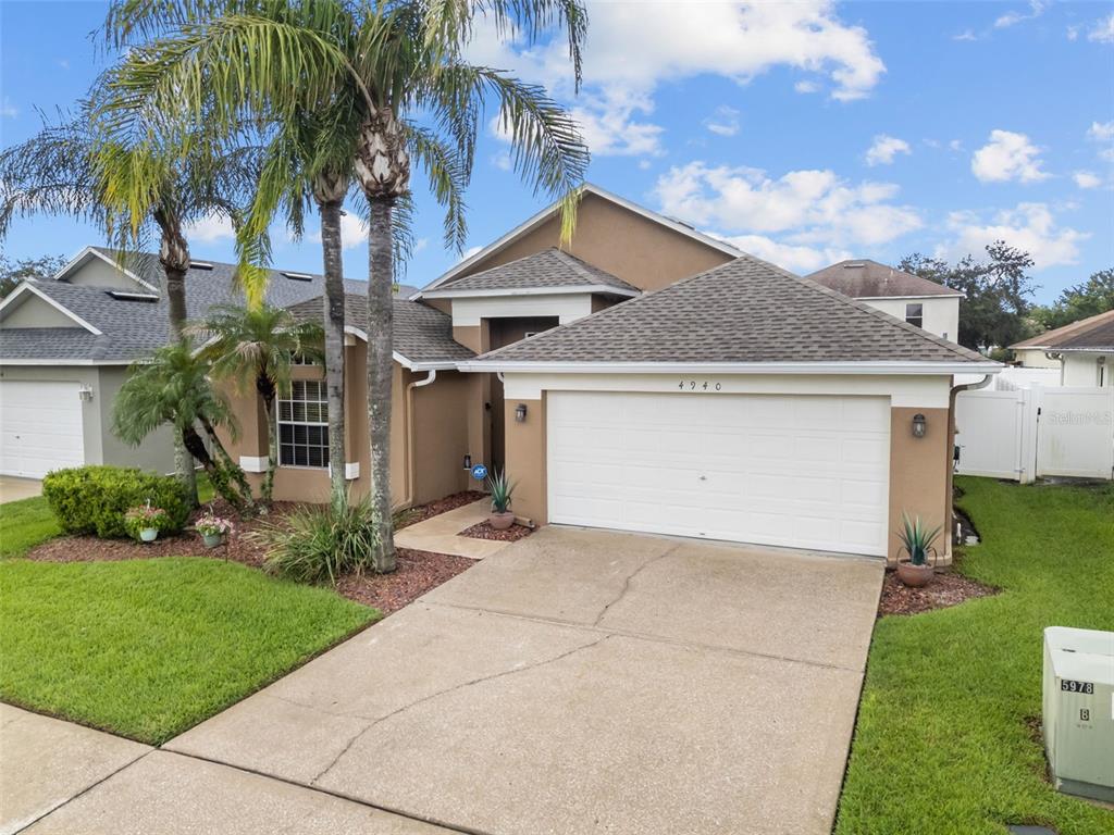 A tan single-story house with a two-car garage, palm trees, and a concrete driveway — 4940 HIDDEN HILLS LANE, WESLEY CHAPEL, FL