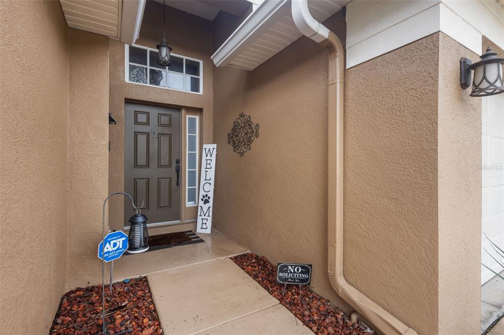 A brown front door with a transom window and a welcome sign on a porch — 4940 HIDDEN HILLS LANE, WESLEY CHAPEL, FL