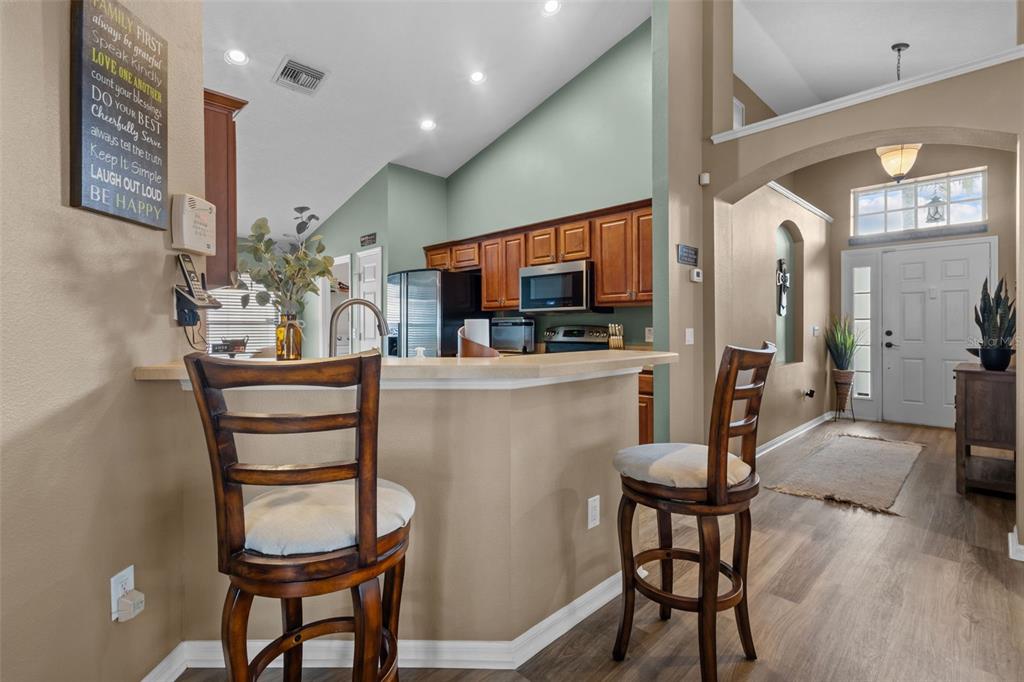 A kitchen with a breakfast bar and stools opens into a foyer with a front door — 4940 HIDDEN HILLS LANE, WESLEY CHAPEL, FL