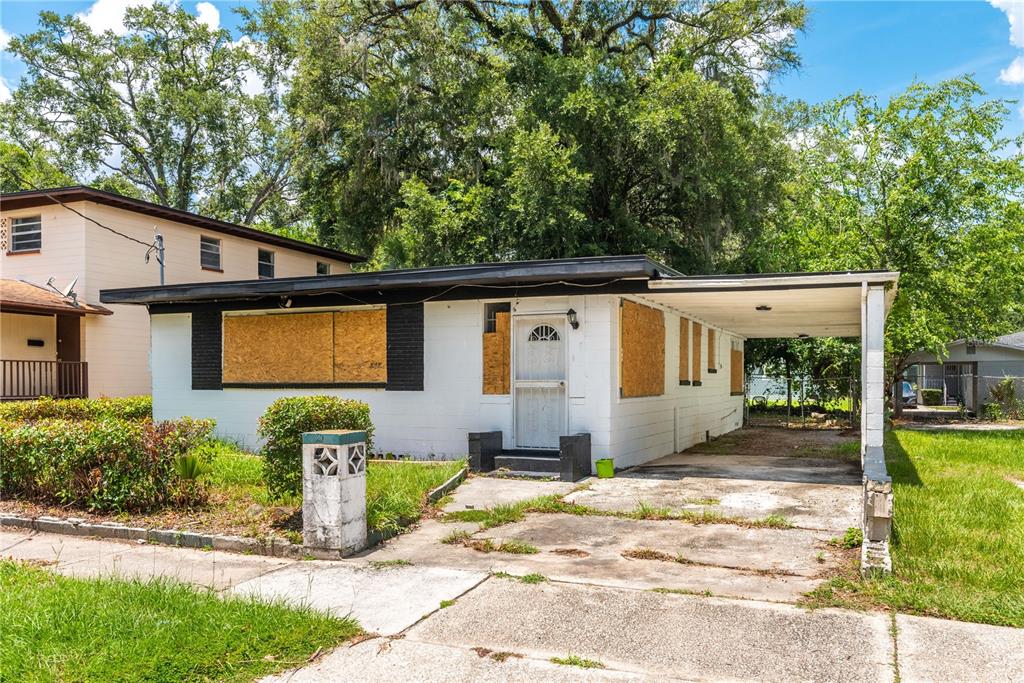A single-story house with boarded-up windows and an attached carport under a large tree — 1651 W 34 STREET, JACKSONVILLE, FL