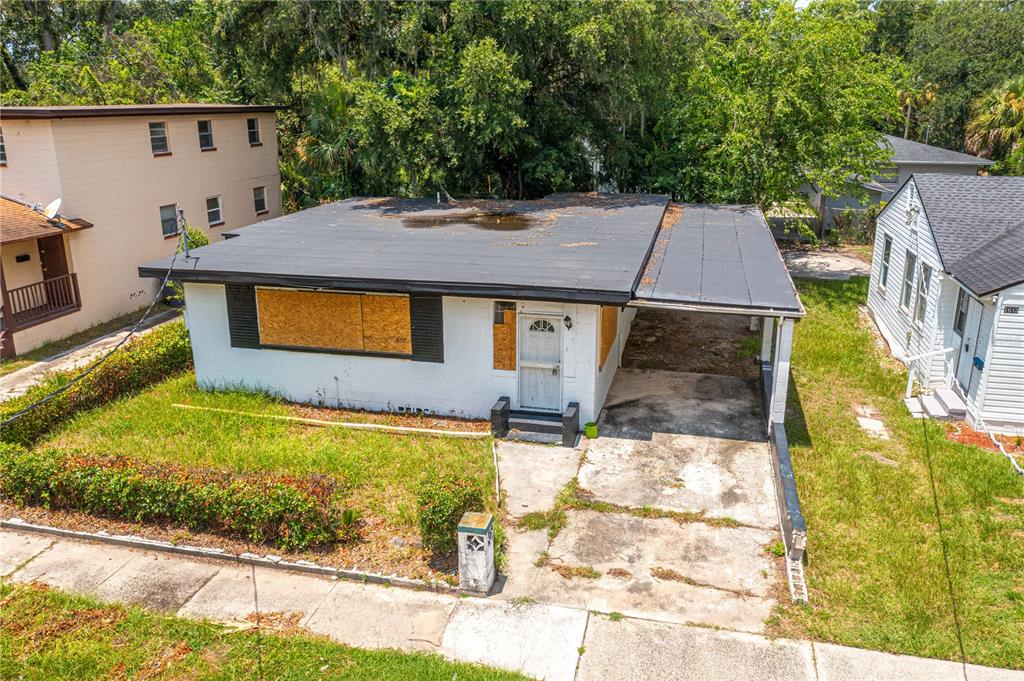 An exterior view of a single-story house with a flat roof, carport, and boarded-up windows — 1651 W 34 STREET, JACKSONVILLE, FL