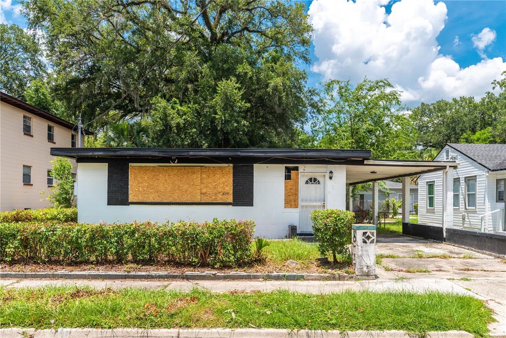 A single-story house with a flat roof, boarded-up windows, and an attached carport — 1651 W 34 STREET, JACKSONVILLE, FL