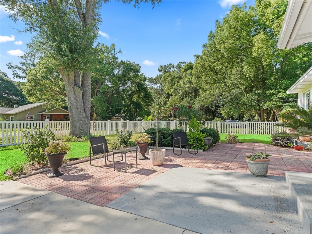 A backyard patio features brick pavers, outdoor seating, potted plants, and a white picket fence — 636 SE 31ST TERRACE, OCALA, FL