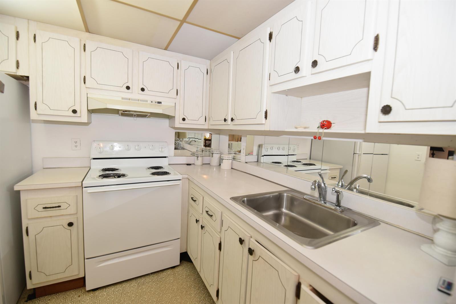 A kitchen features white cabinets, a white electric stove, a stainless steel sink, and mirrors — 715 Saxony O, Delray Beach FL 33446, DELRAY BEACH, FL