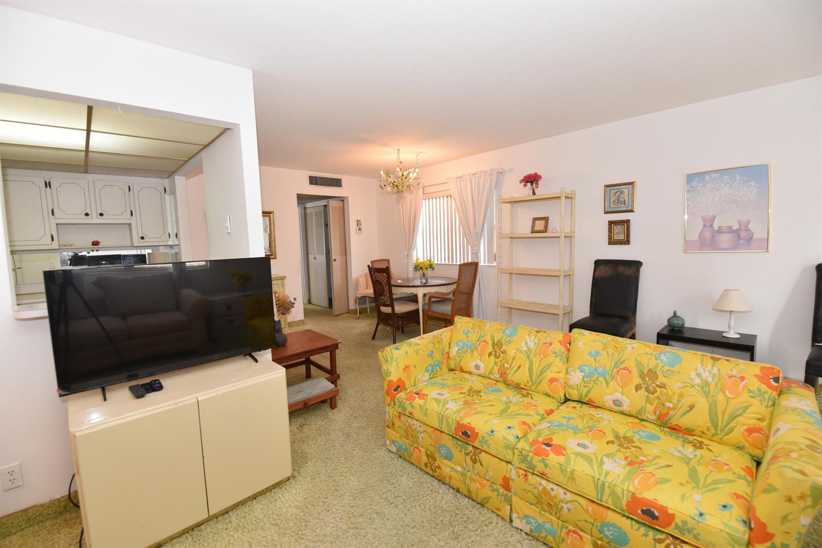 A living room with a floral sofa, green carpet, and an adjacent dining area — 715 Saxony O, Delray Beach FL 33446, DELRAY BEACH, FL