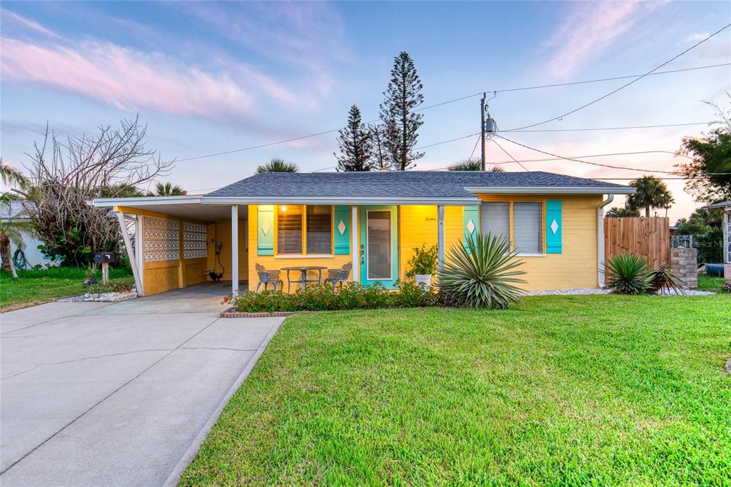 A yellow single-story house with a carport, teal shutters, and a front lawn at sunset — 12 OCEAN SHORE DRIVE, ORMOND BEACH, FL