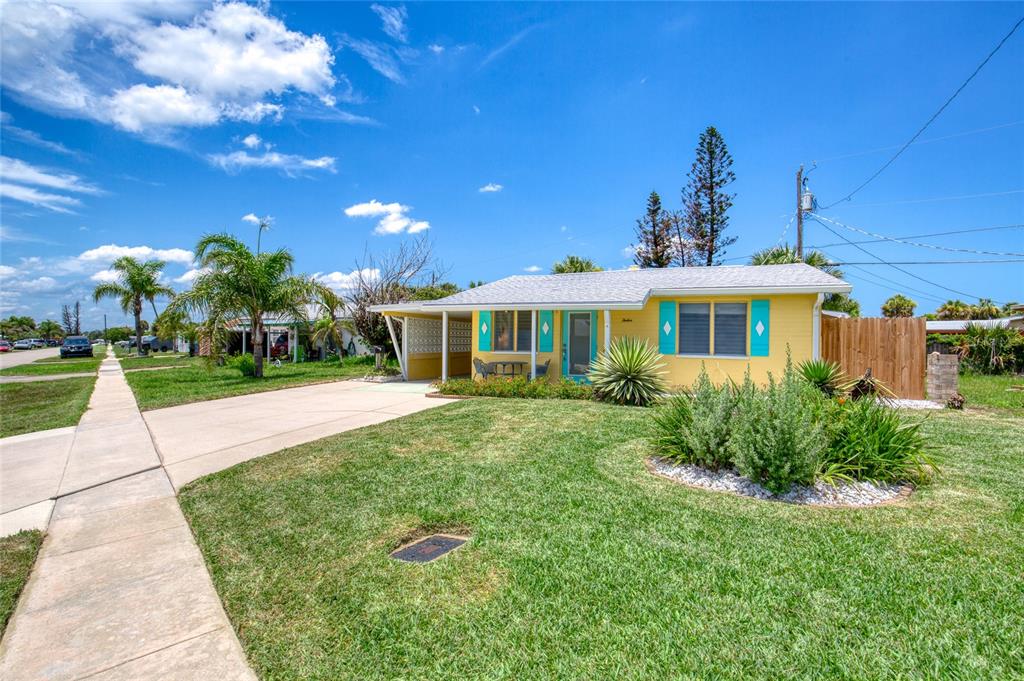 A yellow single-story house with turquoise shutters and a carport sits on a grassy lot — 12 OCEAN SHORE DRIVE, ORMOND BEACH, FL