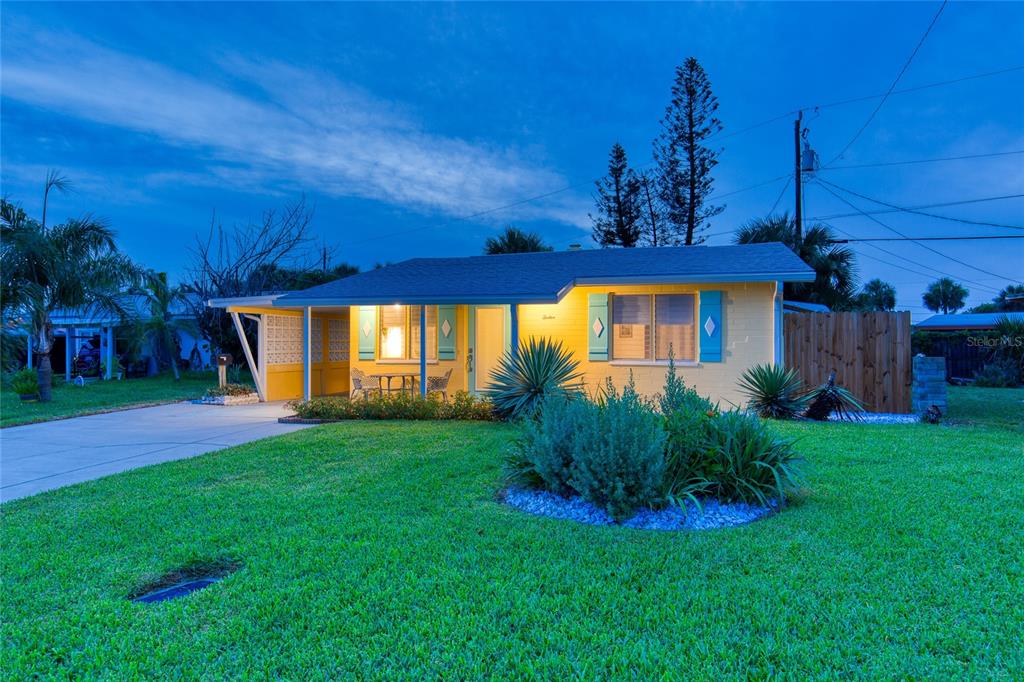 A yellow single-story house with blue shutters and a covered patio at dusk — 12 OCEAN SHORE DRIVE, ORMOND BEACH, FL