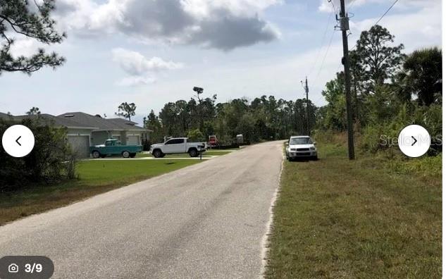 A paved road runs past a residential house with two parked trucks and a white car — 8198 DITMAR STREET, PORT CHARLOTTE, FL