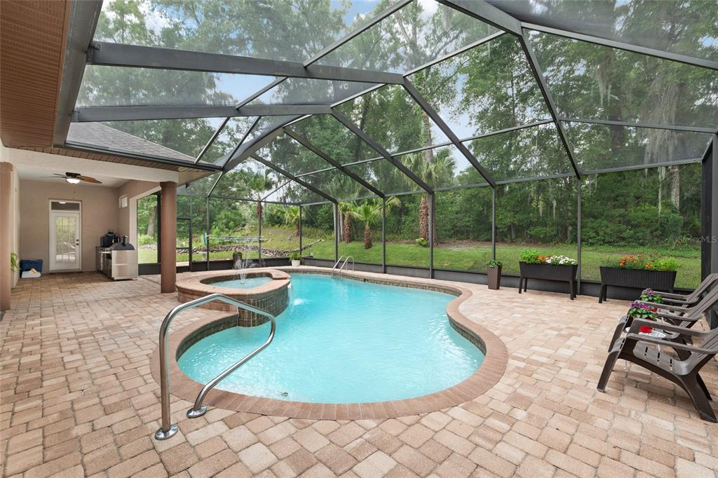 A screened-in patio features a swimming pool with a hot tub and paver flooring — 19654 SW 88TH LOOP, DUNNELLON, FL