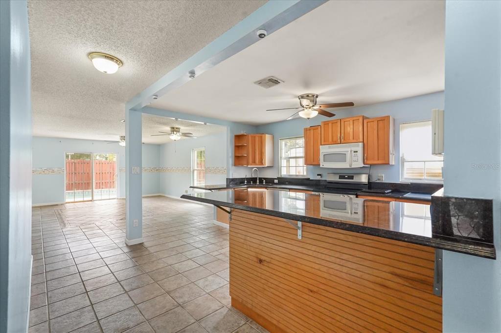 A kitchen with wood cabinets and a breakfast bar opens into a tiled living area — 2019 PAPRIKA DRIVE, ORLANDO, FL