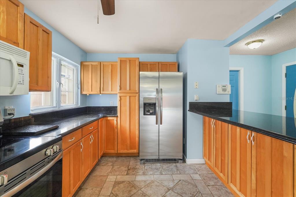 A kitchen features light wood cabinets, black granite countertops, stainless steel appliances, and tile flooring — 2019 PAPRIKA DRIVE, ORLANDO, FL
