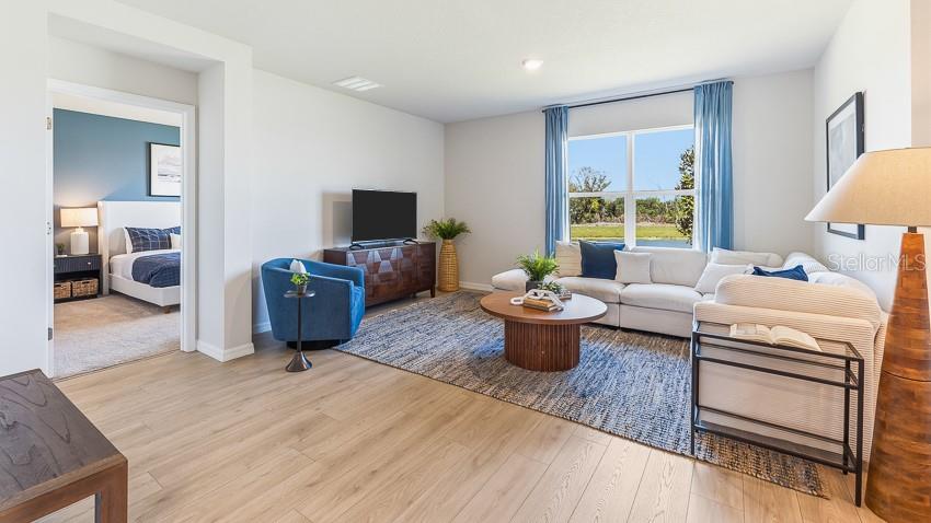A living room with light wood floors, a sectional sofa, and an adjacent bedroom doorway — 2964 FISHERY COURT, LAKEWOOD RANCH, FL