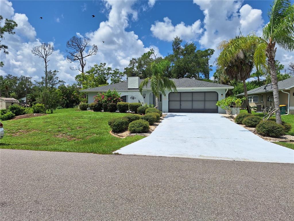 A single-story house with a light-colored exterior, a two-car garage, and a landscaped front yard — 2223 TINKER STREET, PORT CHARLOTTE, FL